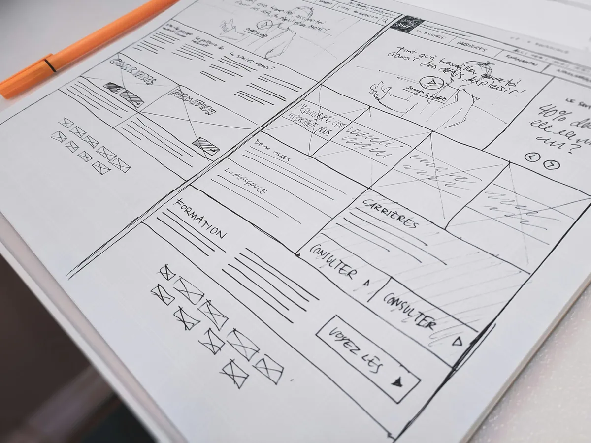 Maquette de site internet dessinée au crayon sur papier, stylo orange posé à côté