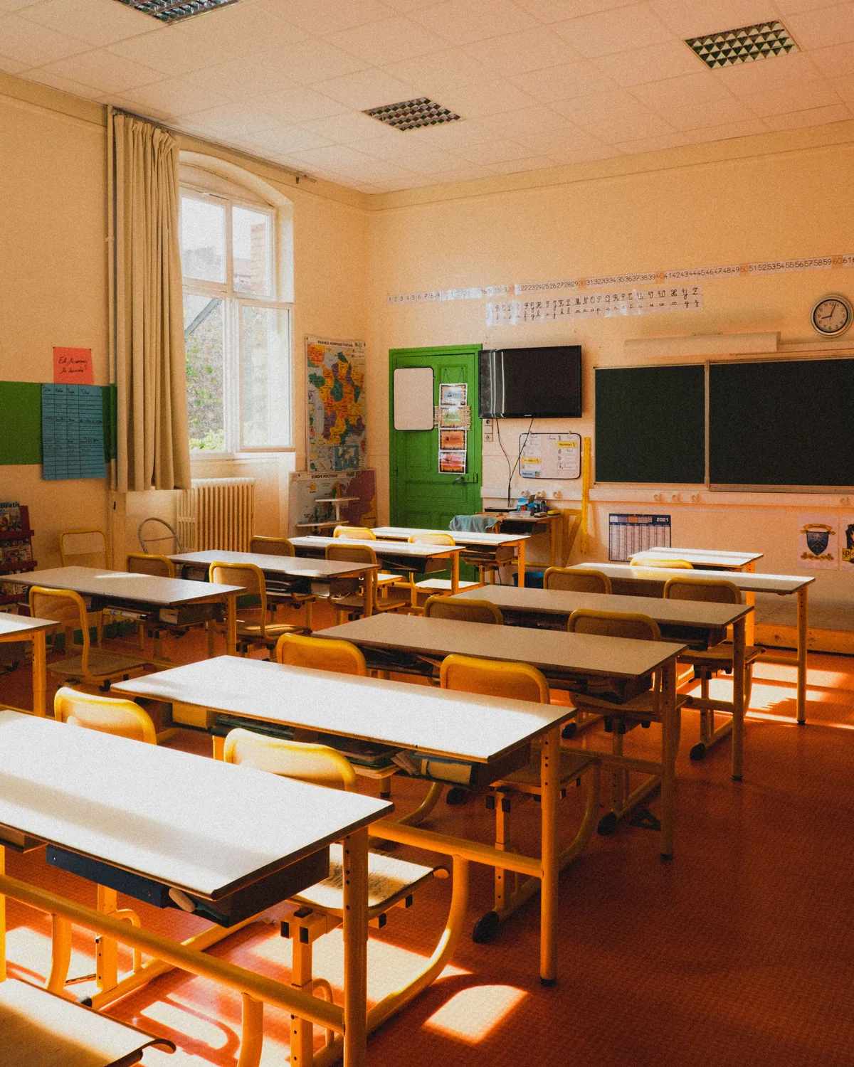 Salle de classe vide d'une école primaire, tables et chaises jaunes, tableau vert, lumière du matin